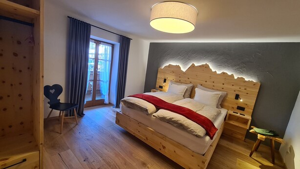 Un letto con struttura in legno, una testiera, un comodino, una sedia e una finestra con tende.