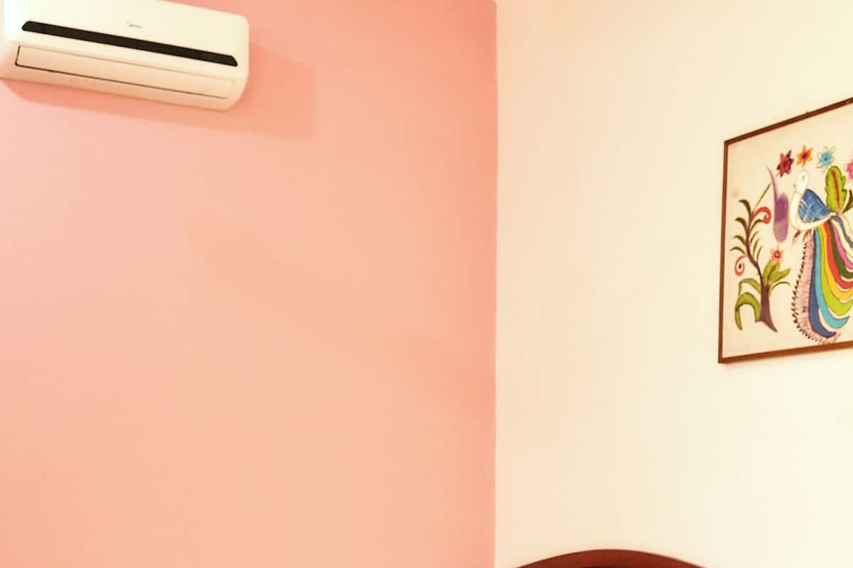 A hotel room with two single beds, a wooden headboard, a wall-mounted air conditioner, and a colorful wall decoration.