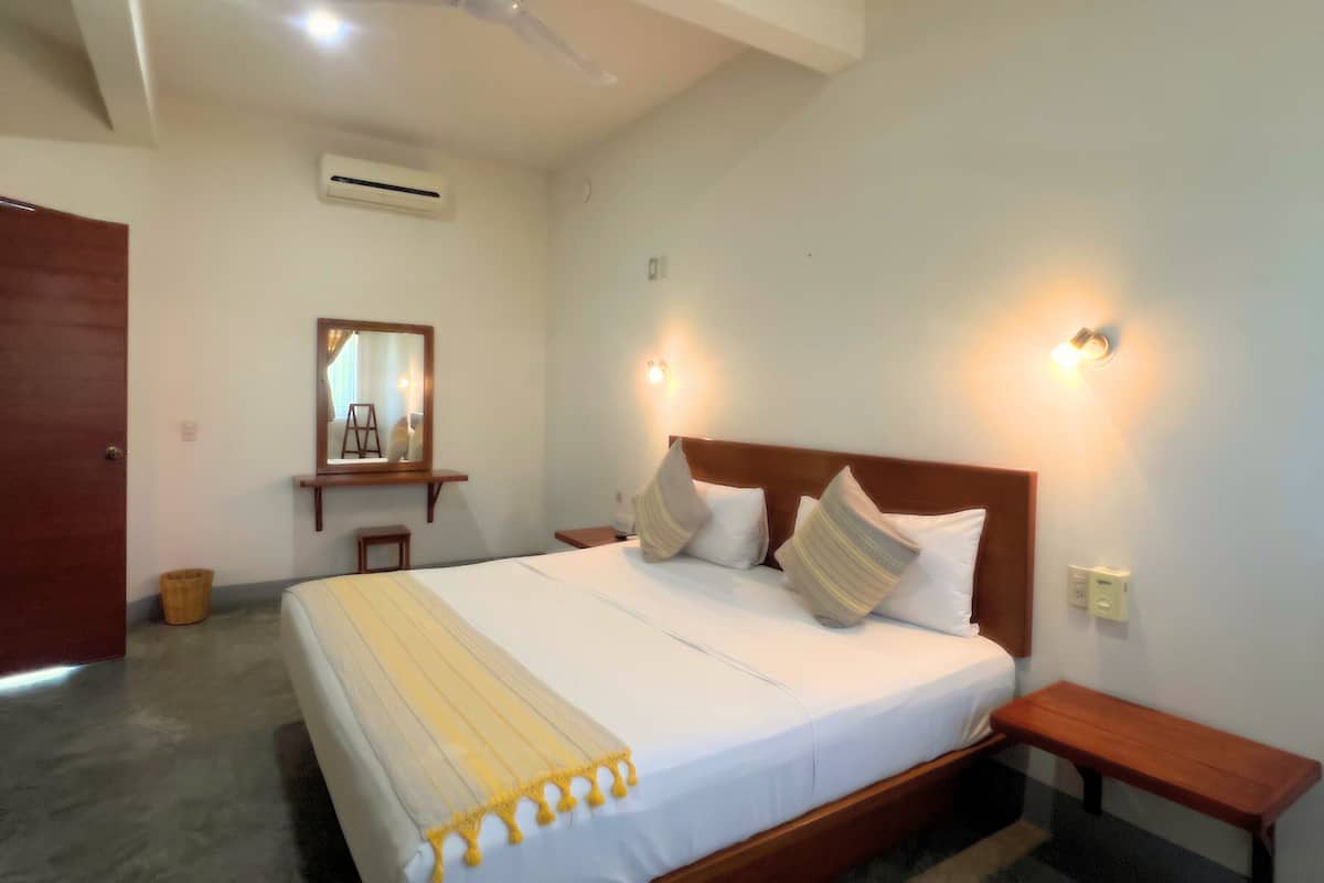 A neatly made bed with a wooden headboard, two bedside tables, a small stool, and a mirror on the wall.