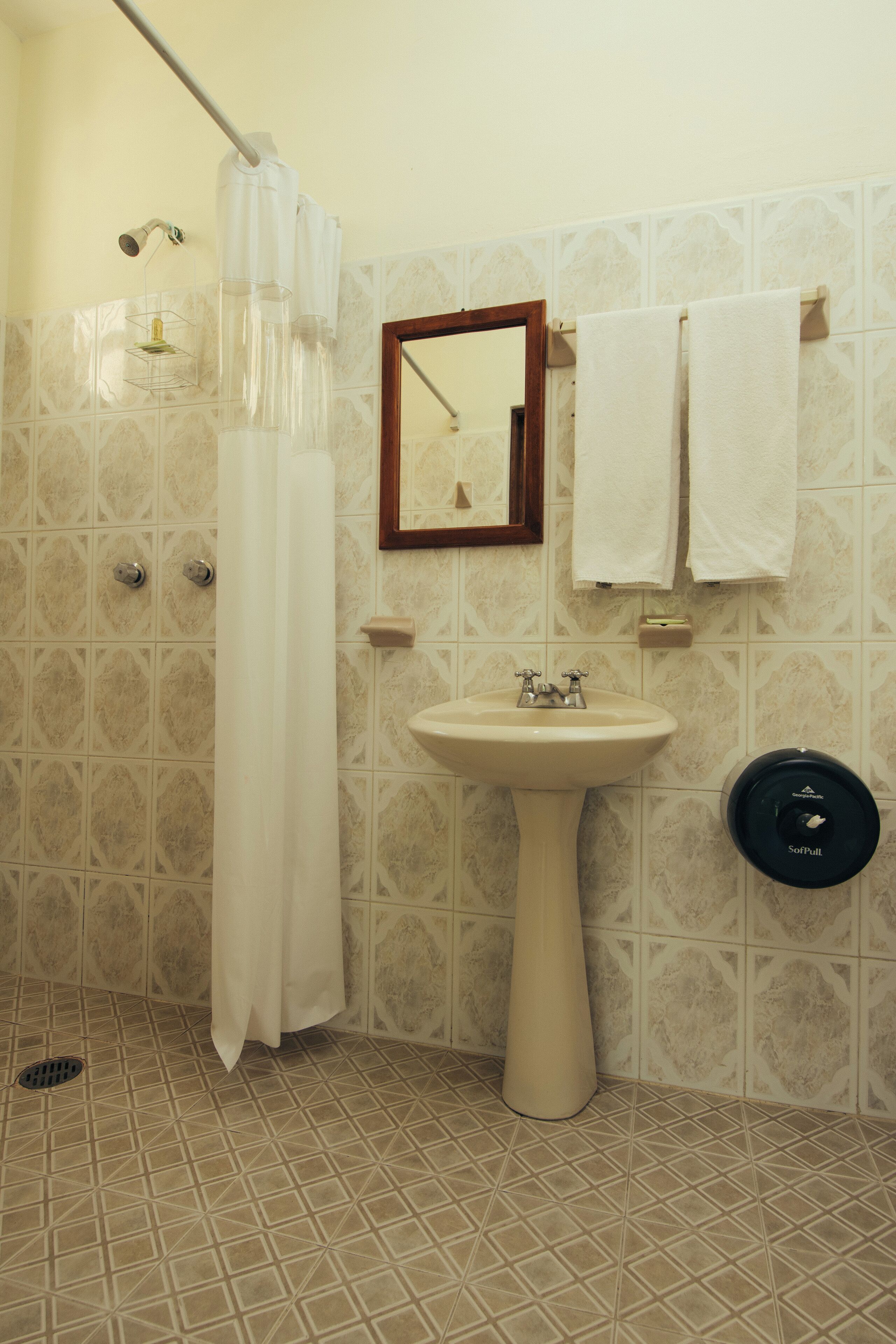 A bathroom with a pedestal sink, a shower with a curtain, a mirror, and two towels hanging on a rack.