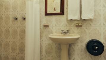 A bathroom with a pedestal sink, a shower with a curtain, a mirror, and two towels hanging on a rack.