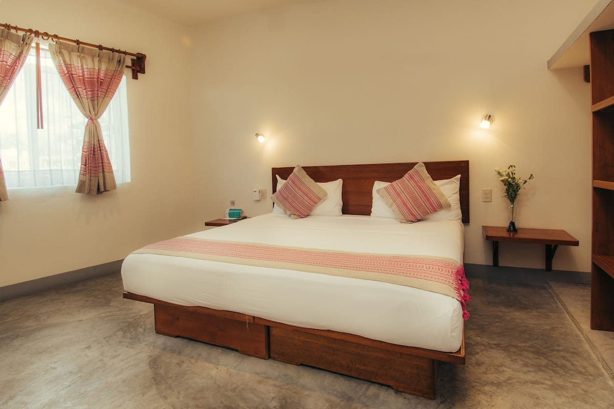 A large bed with a wooden frame, two bedside tables, a nightstand, a small bedside table, and a wall-mounted light fixture.