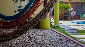 Una hamaca bajo una estructura de madera, un mural en la pared y un edificio con techo de tejas al fondo.