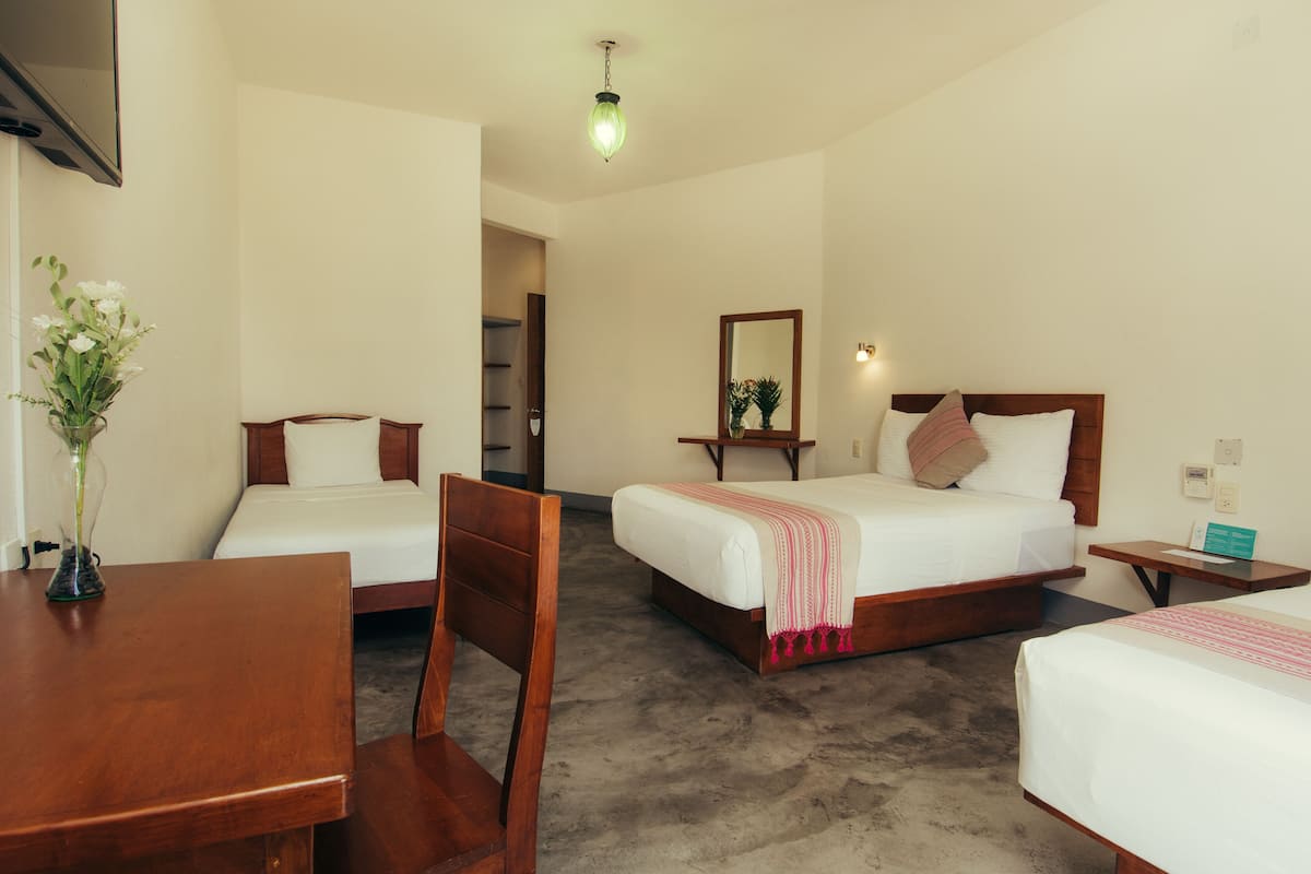 A hotel room with two beds, a wooden table, a chair, a vase with flowers, and a mirror.