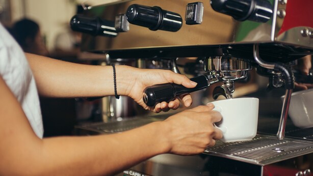 Une personne utilise une machine à expresso et tient une tasse sous le bec verseur.
