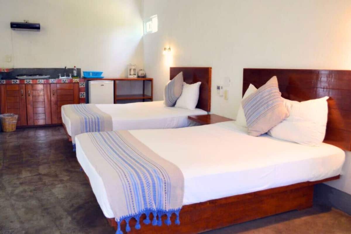 A hotel room with two single beds, a small kitchenette, and a wooden headboard.