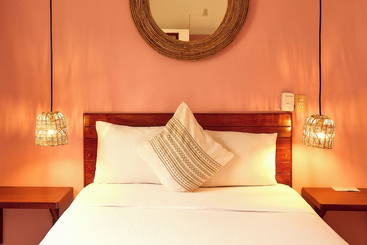 A neatly made bed with a wooden headboard, two bedside lamps, and a wall-mounted mirror.