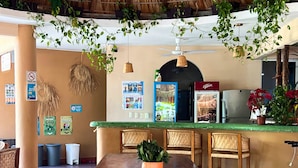 Un restaurant doté d’une grande table en bois, de plantes suspendues, d’un ventilateur de plafond et d’un toit de chaume.