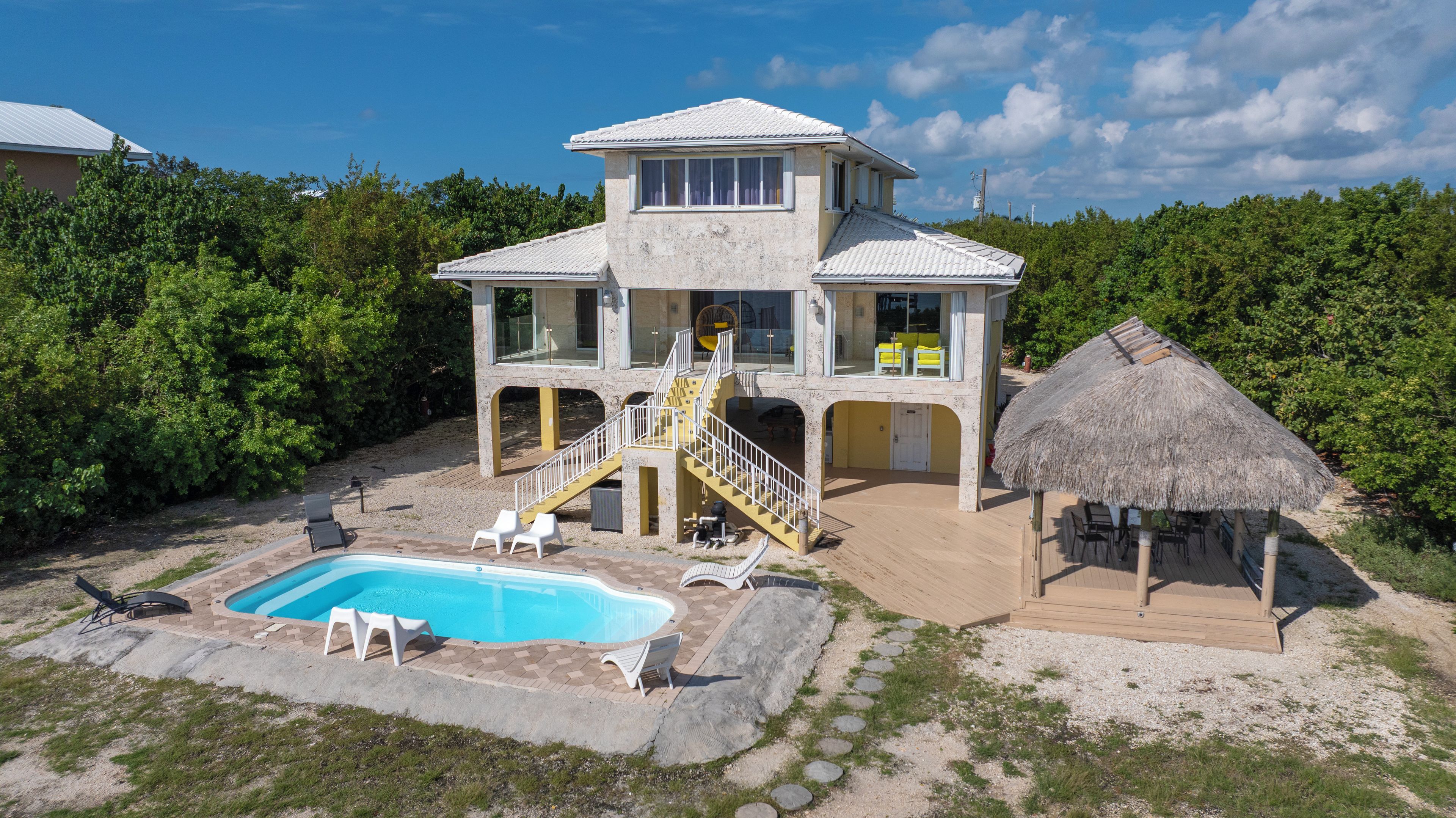 A two-story building with a swimming pool, outdoor seating, and a thatched-roof structure.