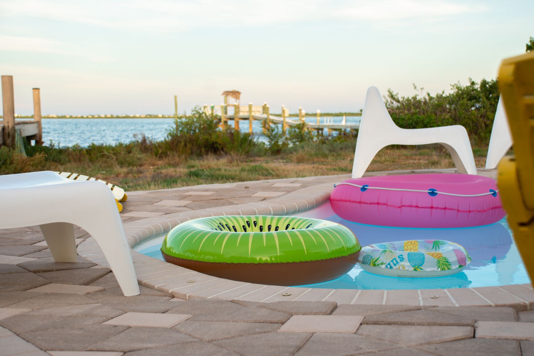 A pool area with three inflatable rings and a white chair.