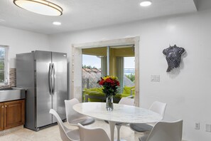 A modern kitchen with a stainless steel refrigerator, a dining area with a white marble table and chairs, and a view through a glass door to an outdoor area. - Keys Beach houses with a daily, rental license. Just remodeled (Summerland Key)