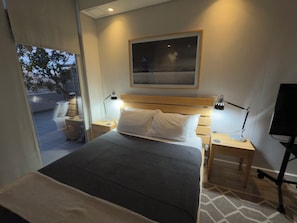 Une chambre d’hôtel comprenant un lit, deux lampes de chevet, une table de chevet, un bureau, une chaise et une fenêtre donnant sur l’extérieur.