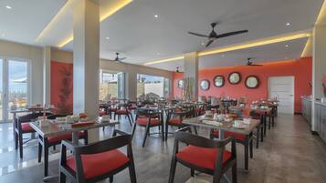 A spacious dining area with multiple tables and chairs, large windows, and ceiling fans.