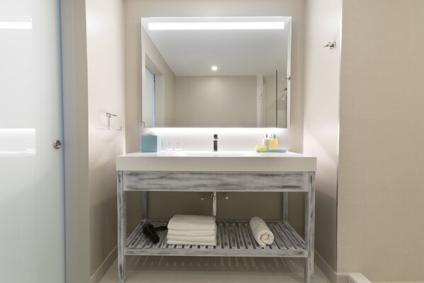 Un baño con un lavamanos blanco, un espejo encima y un estante debajo.