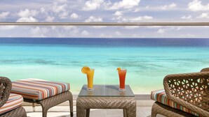Un salón junto a la playa con mobiliario de mimbre y una mesa de vidrio, con vistas a un mar turquesa.