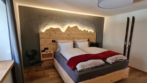 Uma cama de madeira com cabeceira, uma mesa de cabeceira, uma cadeira e esquis na parede.