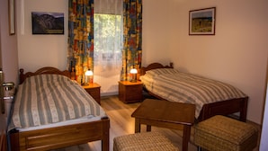 Un dormitorio con dos camas individuales, una mesa de madera, una silla y una ventana con cortinas estampadas.