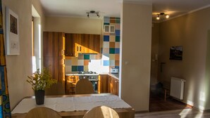 Un comedor con mesa y sillas de madera, una planta en maceta y vista a la cocina.
