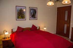 A bedroom with a wooden bed, red bedding, two framed pictures on the wall, a nightstand with a lamp, and a wooden door. - Tranquility, nature and recreation at the Schneekoppe, ideal for hiking or winter sports. (Karpacz)