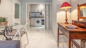 A compact living space with a dining area, a kitchen with a washing machine, and a wooden dresser with a mirror. - Quiet and elegance in the Andalusian capital 4 px-WIFI (Sevilla)