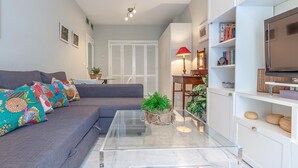 A modern living room with a grey sofa, colorful cushions, a glass coffee table, a red lamp, a TV, and a bookshelf. - Quiet and elegance in the Andalusian capital 4 px-WIFI (Sevilla)