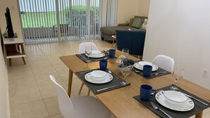 A dining area with a wooden table set for four, white chairs, and a blue sofa in the background.