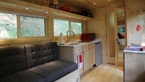 Una cocina compacta con un banco tapizado de gris, armarios de madera, un microondas y un lavamanos.