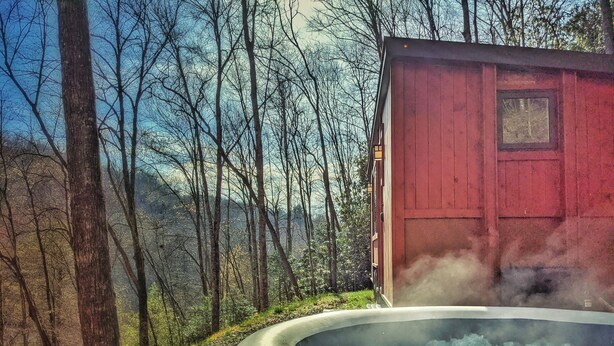 Una cabaña rústica con jacuzzi en un área boscosa.