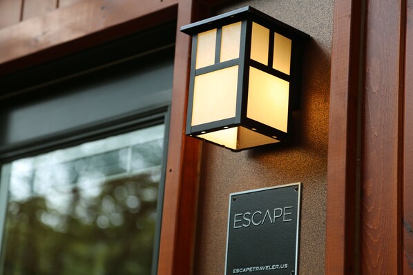 A black sign with white lettering reading "ESCAPE" and "ESCAPETRAVELER.US" mounted on a wooden wall.
