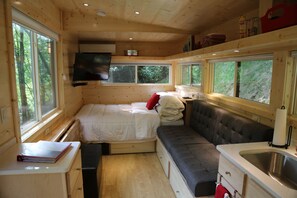 Cozy cabin with a bed, sofa, kitchenette, and TV, offering forest views.