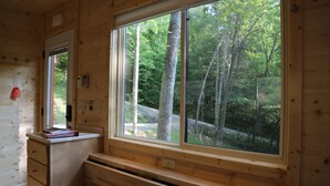 Una cabaña de madera con un ventanal grande que ofrece vistas a un bosque. Se observa un escritorio con cajones y un objeto rojo encima.