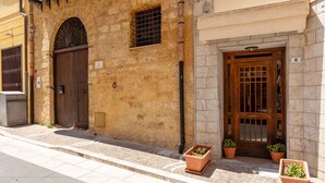 Un edificio con fachada de piedra, una puerta de madera con un ventanal y dos macetas con plantas en el suelo.