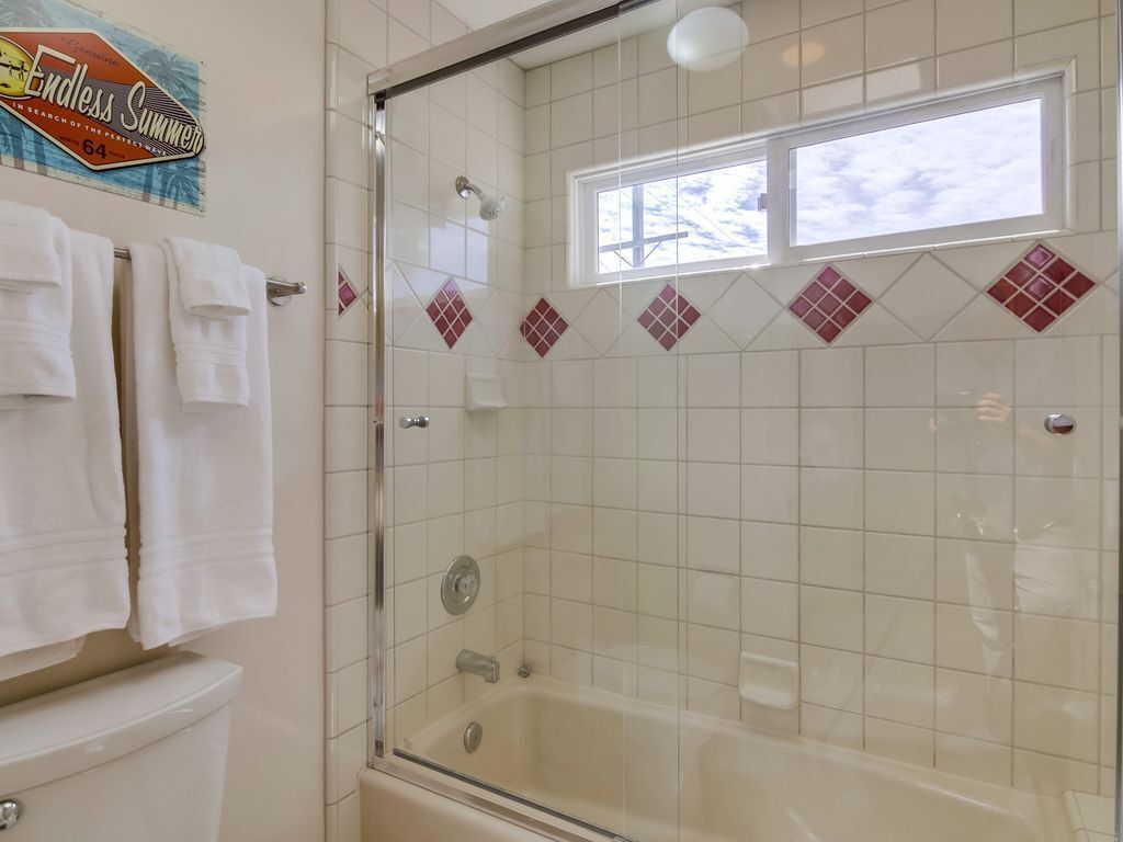 Un baño con ducha envuelta en vidrio, azulejos blancos y una ventana sobre la bañera.