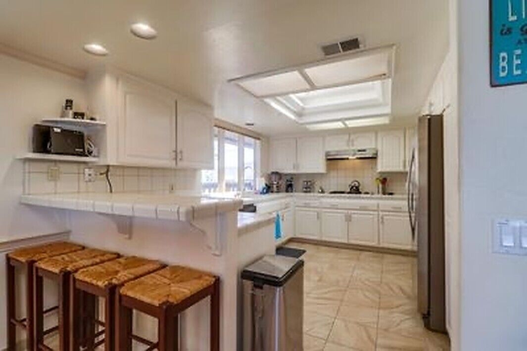 A kitchen with white cabinets, a countertop, and a trash bin.