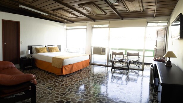 Une chambre d’hôtel avec un lit, une chaise, un bureau et un balcon équipé de chaises.