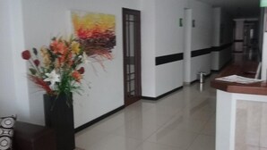 Un couloir avec un comptoir d’accueil, un vase de fleurs et une peinture abstraite aux couleurs vives accrochée au mur.
