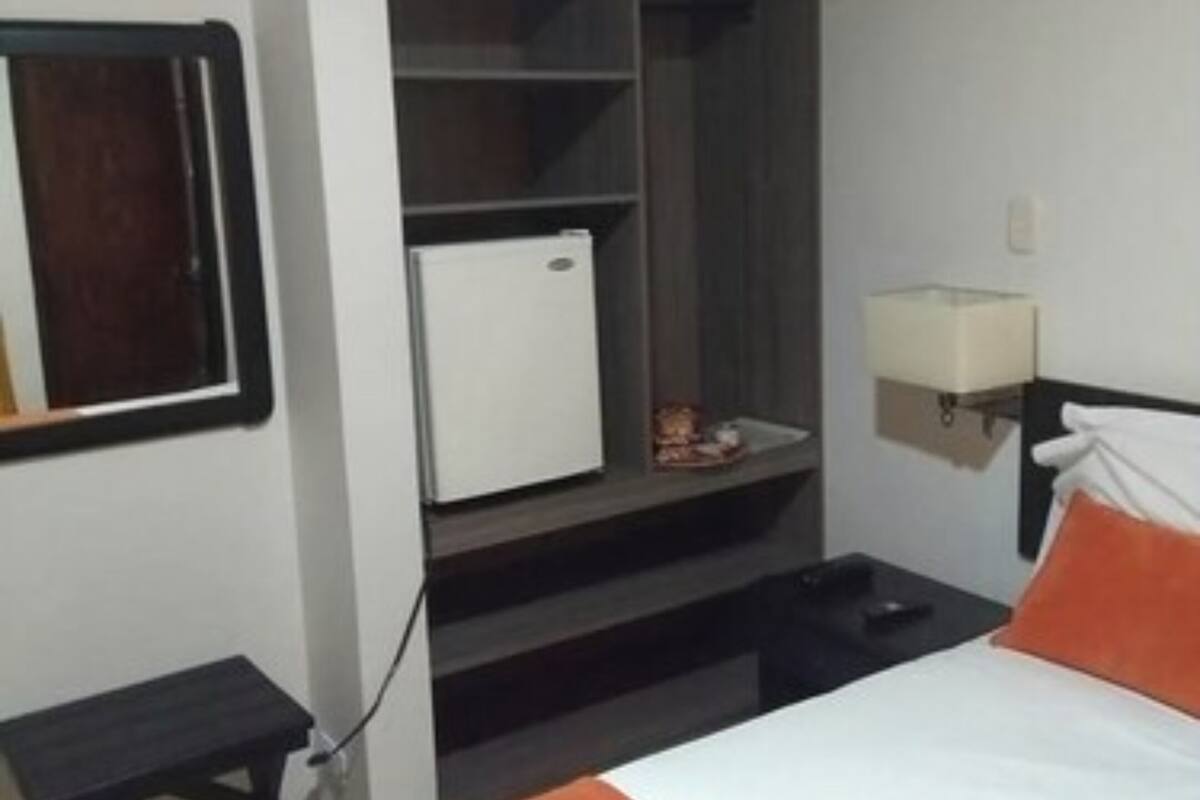 Une chambre d’hôtel avec un lit, un petit bureau, une armoire et une table de chevet.
