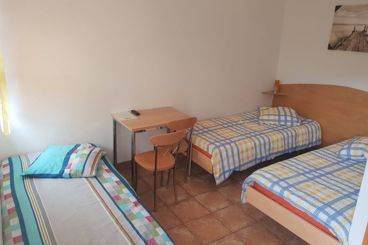 A dormitory room with two single beds, a desk, and a chair.