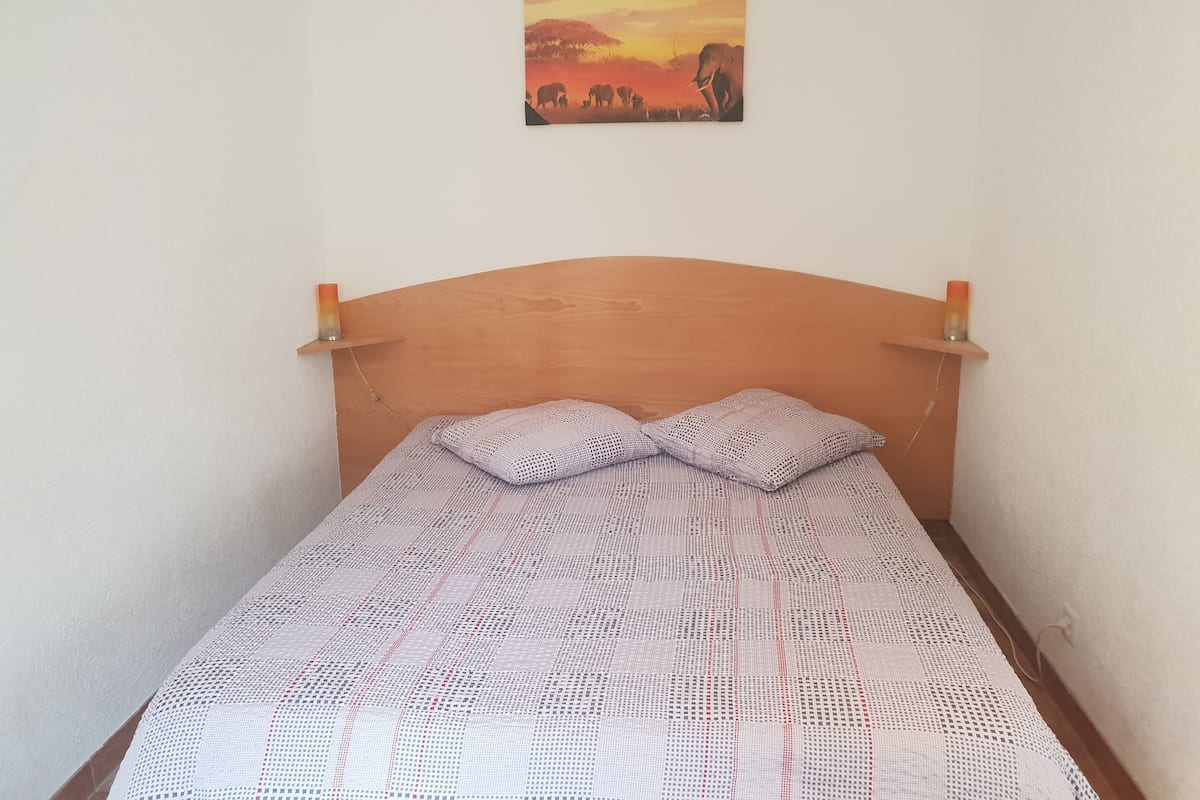 A single bed with a wooden headboard, a patterned bedspread, and a sunset painting above it.