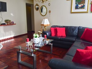 A modern living room with a black leather sofa, red cushions, a glass coffee table, and decorative items including a vase with flowers and a lamp.