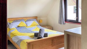 A bedroom with a wooden bed, a nightstand, a bedside lamp, and a window with curtains.