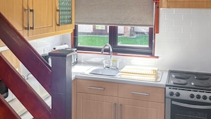 A compact kitchen with wooden cabinets, a built-in oven, a sink, and a window with a view of a green lawn.