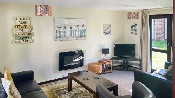 A living room with a TV, sofa, and coffee table. There are wall decorations and a window with curtains.