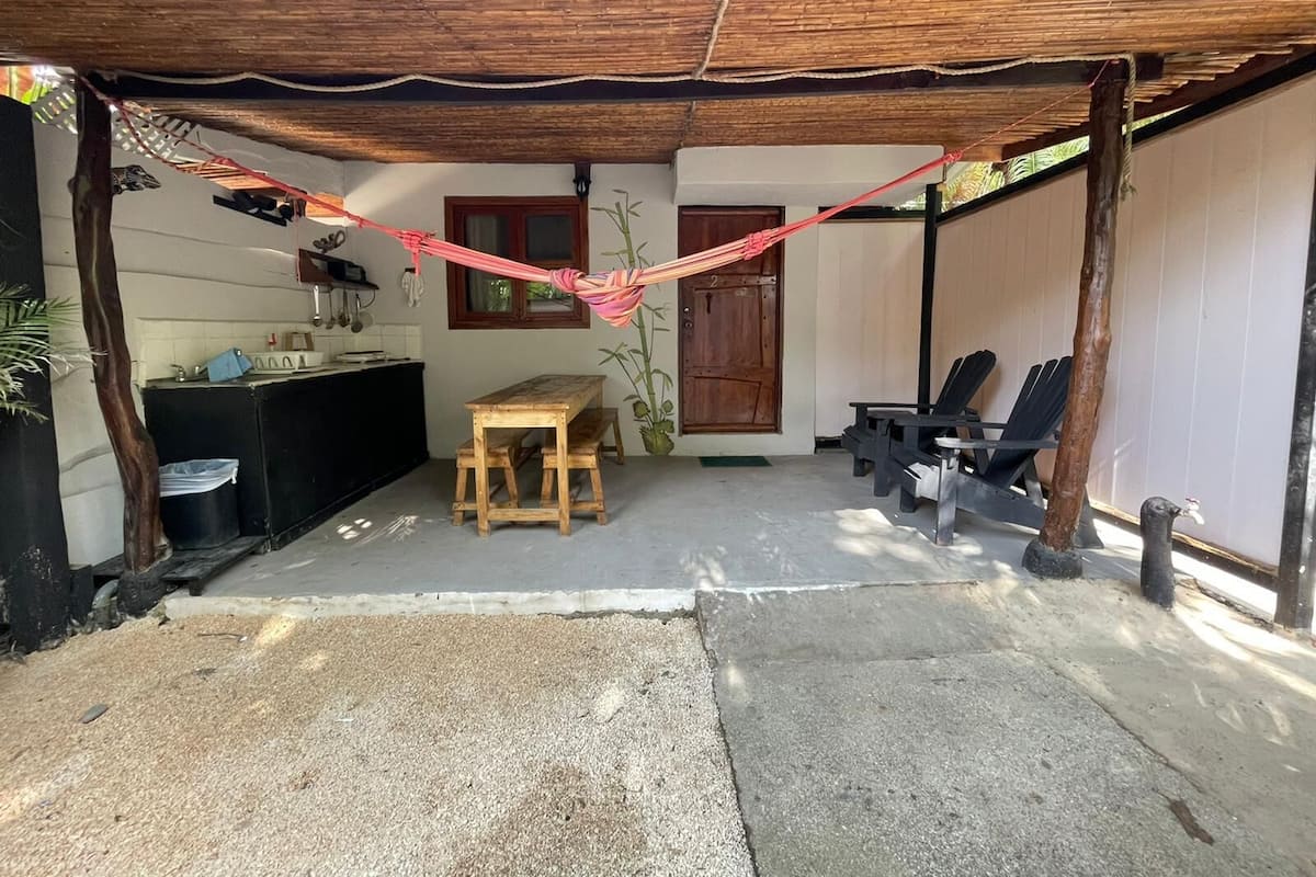A covered outdoor area with a wooden table and chairs, a hammock, and a door.