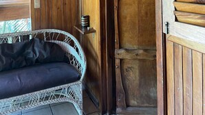 A wooden cabin interior with a wicker sofa, a wooden door, and a metal shelf. - Beach Cabinas (Cóbano)