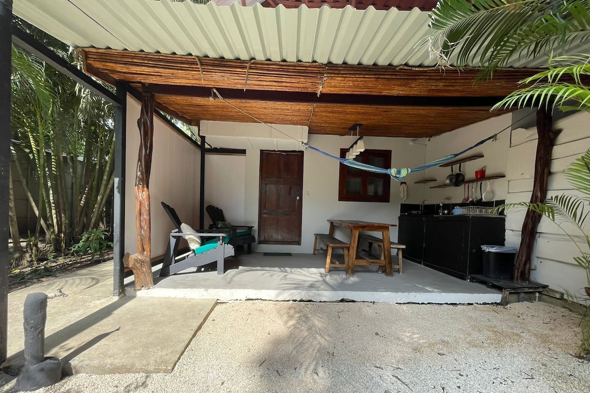 A covered outdoor seating area with a table and chairs, a hammock, and a kitchen area with cabinets and utensils.