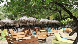 A beachside seating area with wooden benches and tables, surrounded by thatched umbrellas. - Beach Cabinas (Cóbano)