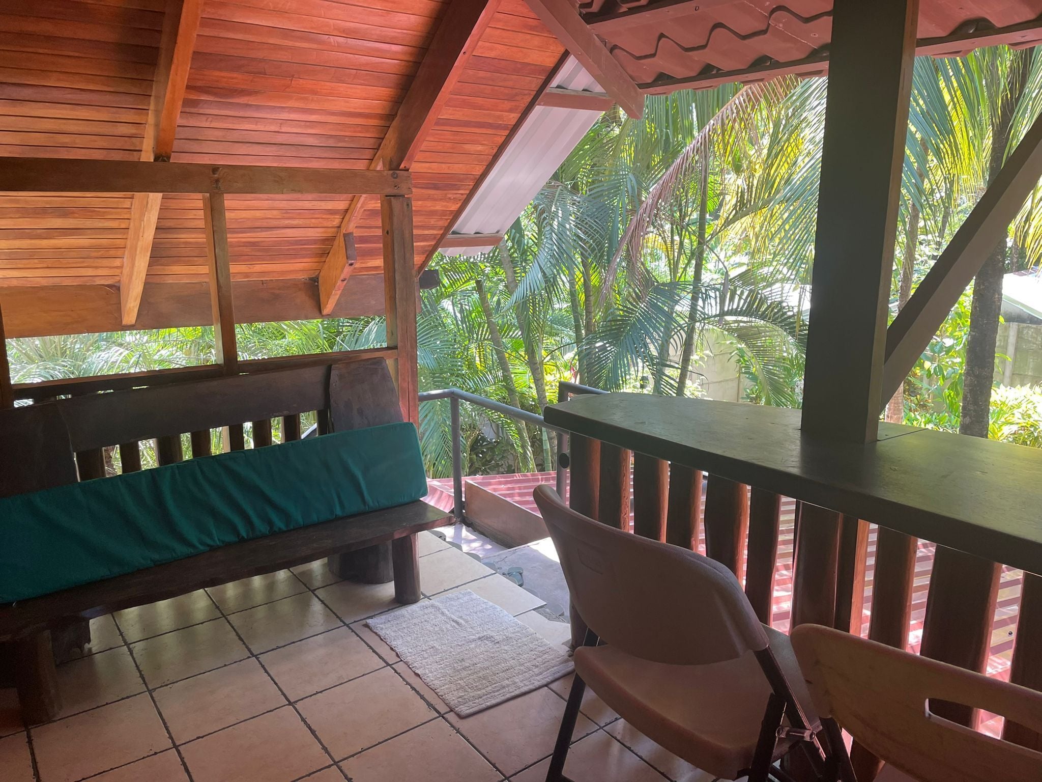 Una terraza de madera con un banco y una silla, rodeada de exuberante follaje.