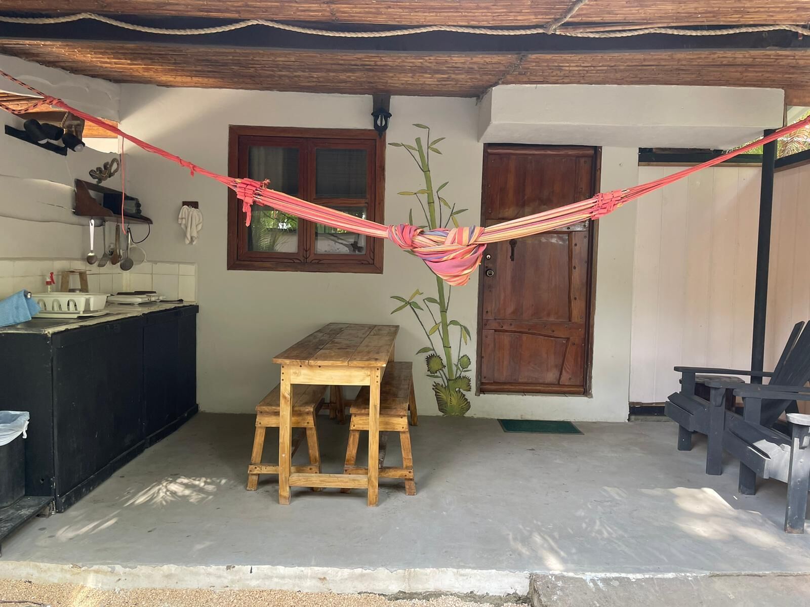 A rustic kitchen with a wooden table and bench, a hammock, and a door.