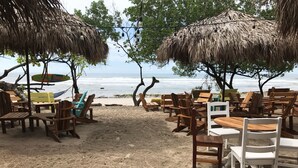 A beachside seating area with wooden tables and chairs, thatched umbrellas, and a sign reading "Royal Beach". - Beach Cabinas (Cóbano)
